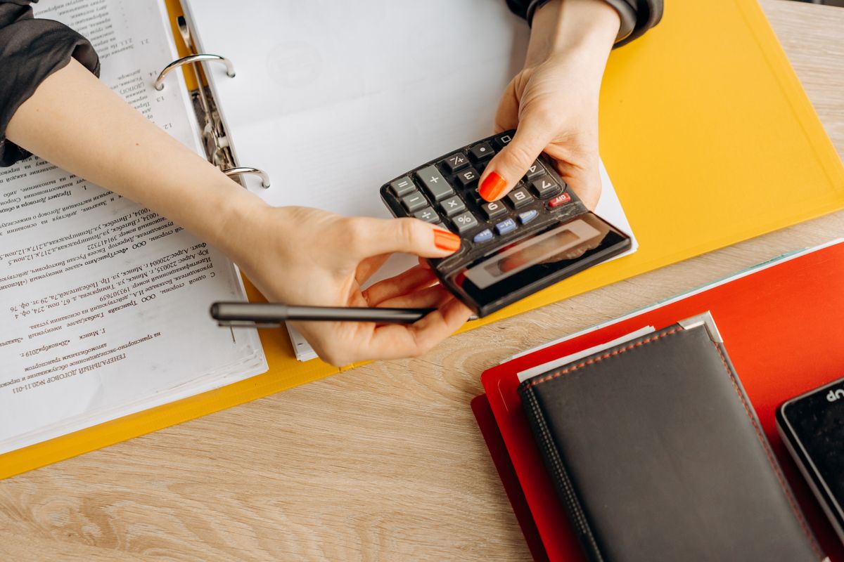 Manos usando una calculadora sobre un escritorio con documentos y carpetas, en el contexto de evaluar el costo y el riesgo de contratar a un monotributista