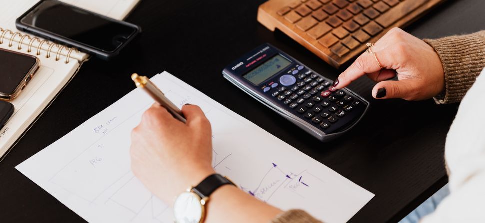 Escritorio con calculadora y documentos – regularizacion de empleados Manos revisando documentos y usando una calculadora sobre un escritorio, en el contexto de la regularización de empleados no registrados